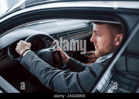 Looking through the opened window. Lovely successful couple trying new car in the automobile salon Stock Photo
