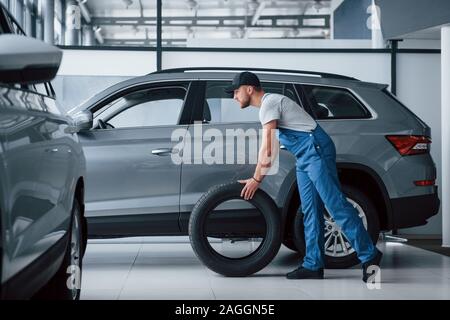Working day. Mechanic holding a tire at the repair garage. Replacement of winter and summer tires Stock Photo