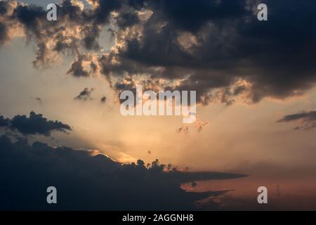The sun setting behind dark clouds, sun rays and colorful sky Stock Photo