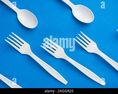 Plastic white disposable fork and spoon on a trendy blue color background. Concept plastic dishes, fast food, plastic pollution. Top view, flat lay. Stock Photo