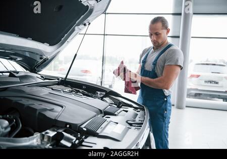 Searching for problems. Man in blue uniform works with broken car. Making repairings Stock Photo
