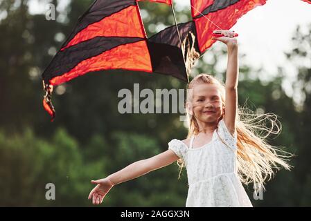 Young kid. Happy girl in white clothes have fun with kite in the field. Beautiful nature Stock Photo