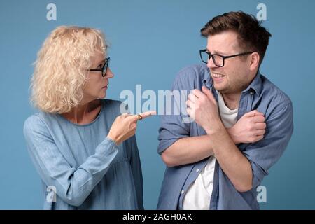 Angry mature woman shouting, blaming millennial annoyed son in eyeglasses. Stock Photo