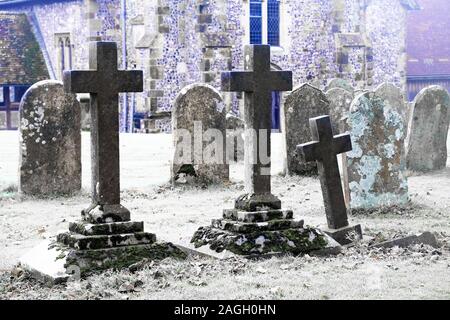 An eary scarey English grave yard with about twenty grave stones, the three headstones in the foreground are in the shape of large Cristian crosses, i Stock Photo