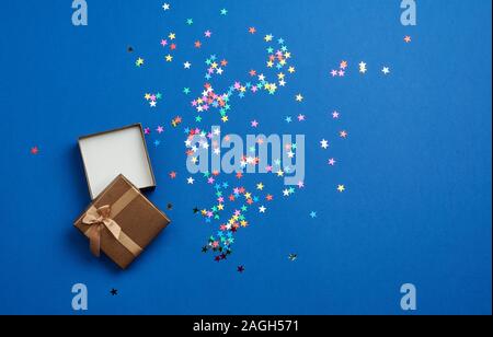 open square empty gift box on a blue background, near multi-colored sequins, top view, festive backdrop Stock Photo