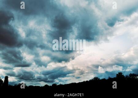 dramatic cloudy sky before a storm, with tops of trees in silhouette Stock Photo