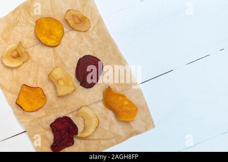 Mixed healthy vegetable chips on cooking paper on white wooden background. Stock Photo