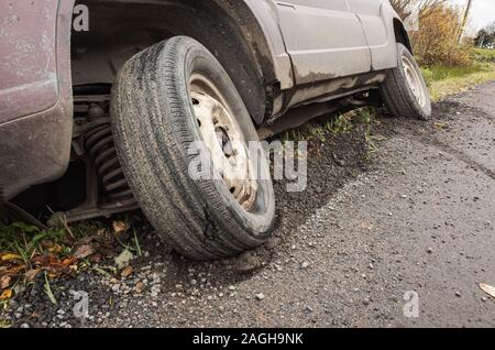 A car in an accident lies in a ditch by rural road at daytime, close up photo ow front wheel Stock Photo