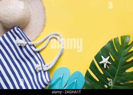 Female beach straw sunhat, outfit, flip flops, beach bag, tropical monstera on yellow. Top view. Summer travel concept. Top view and space for text. Stock Photo