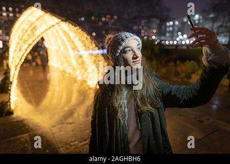 London, UK. 19th December, 2019. Winter Light Art: Student Rebecca, 20, takes a selfie photo of Grosvenor Square's fairy light tunnel. Credit: Guy Corbishley/Ģ����ý Live News Stock Photo
