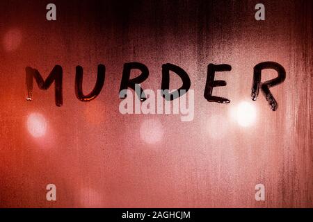 the word murder handwritten on wet glass of night window with bloody red back light of street lights. Stock Photo