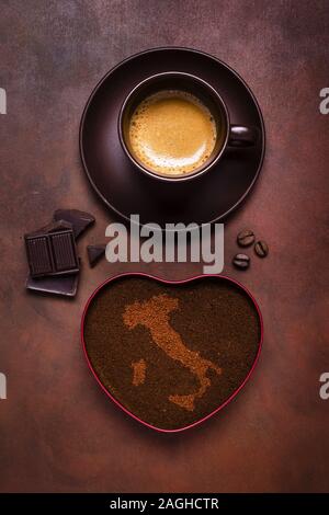 composition with a cup of espresso, a bowl of ground coffee and embossed the shape of Italy Stock Photo