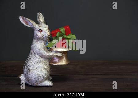 Close-up of a white-golden statuette of an Easter bunny holding a red gift box, Easter background or concept, selective focus Stock Photo
