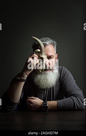 Dark portrait of a bearded middle-aged man with an animal skull, selective focus Stock Photo