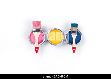 Renovation picture. Isolated white background with three pink, yellow and classic blue pain cans and two brushes, central composition. Flat lay, top v Stock Photo