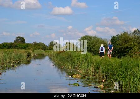 People walking along Wicken Lode River, Wicken Fen Nature Reserve, Wicken, Cambridgeshire, UK Stock Photo