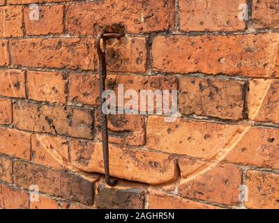 Old swinging rusty iron gate hook / stay which has worn a circular arc groove in an old red brick wall, UK Stock Photo