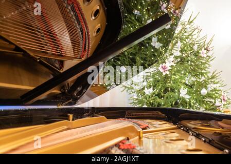 Golden piano interior with visible strings and reflection. In the background a Christmas tree decorated with ornaments and lights. Stock Photo