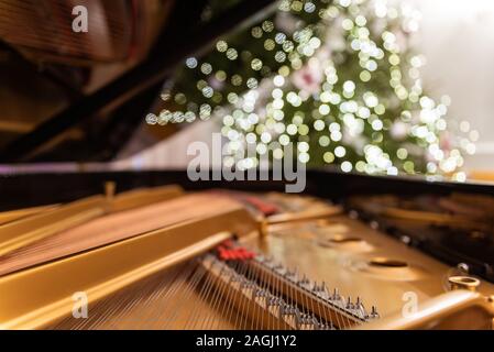 Golden piano interior with visible strings in the foreground. In the background a blurred Christmas tree decorated with ornaments and lights. Stock Photo