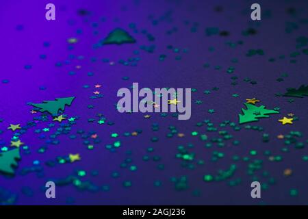 Christmas frame composition with golden star-shaped sequins and pine trees on blue holographic background. Celebration preparation concept. Selective Stock Photo