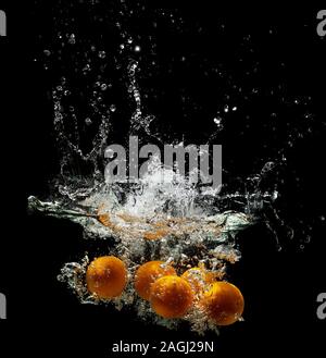Five fresh oranges falling in water on a dark background Stock Photo