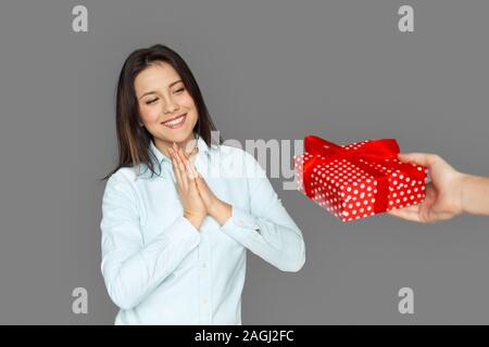 Freestyle. Young woman standing isolated on grey getting present from man smiling surprised Stock Photo