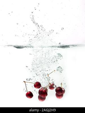 fresh cherries falling in water on a white background Stock Photo