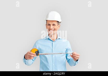 Construction. Mature man in hardhat standing isolated on white with magnetic tape measure smiling cheerful Stock Photo