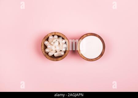Collagen in capsules and in powder in two wooden bowls on pastel pink background Stock Photo