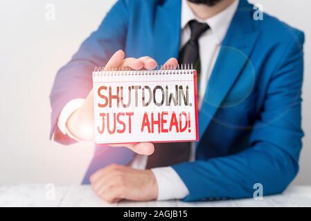 Conceptual hand writing showing Shutdown Just Ahead. Concept meaning closing factory business either short time or forever Man holds empty paper with Stock Photo