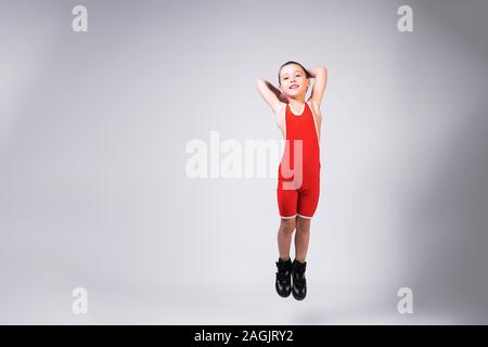 Little funny boy in a red sports ortsovskoy leotard and wrestling boots cheerfully jumps arms up and smiles at his achievements on a white isolated ba Stock Photo