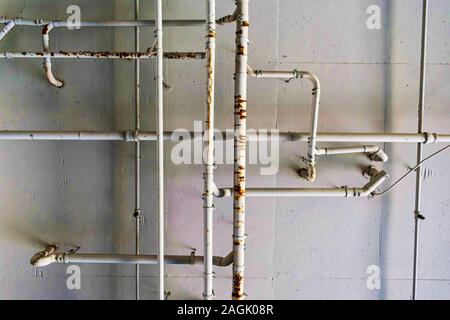 Metal plumbing system and water pipes on cement ceiling. Rusty leaking pipeline and plumbing maze on painted cement ceiling. Stock Photo