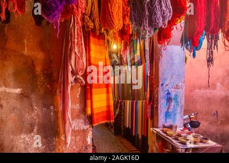 Vibrant color outside a tourist shop in Morocco, with colorful scarves, yarn and paint pigment on textured walls. In the medina of Marrakech. Stock Photo