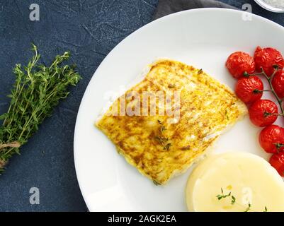 Fish cod baked in the oven with mashed potatoes, tomatoes, diet healthy food. Dark gray background, top view Stock Photo