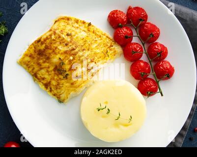 Fish cod baked in the oven with mashed potatoes, tomatoes, diet healthy food. Dark gray background, top view Stock Photo