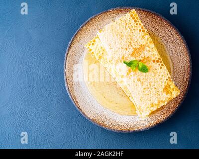 one plate with honey in honeycomb, close-up, on brown ceramic plate, on blue stone table, top view, flat lay. Stock Photo