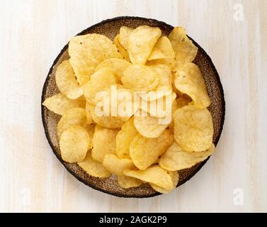 brown yellow chips from natural potato in brown ceramic plate on a white wooden background, top view, close-up Stock Photo