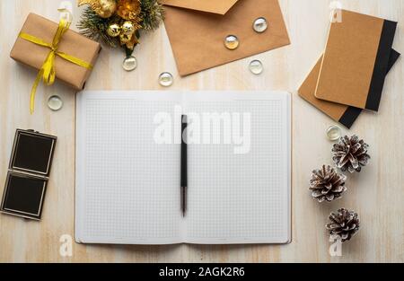white open notepad, kraft envelope, and Christmas decoration lying on a beige wooden background, flat lay, copyspace Stock Photo