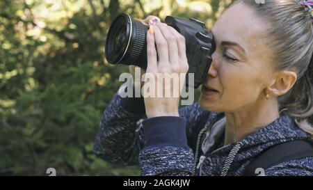 Traveler photographing scenic view in forest. One caucasian woman shooting close up look. Girl take photo video on dslr mirrorless camera. Stock Photo