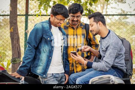 Students busy on mobile at college parking area on bike - Young millennials busy on phones and technology - concept of friendship and urban youthful Stock Photo