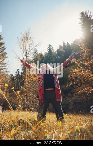 Senior homeless man in torn sweater celebrating life standing in nature lifting his violin high up in the air. Stock Photo