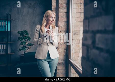 Profile side photo of dreamy peaceful middle aged woman freelancer have break hold mug with espresso look window think about future briefings with Stock Photo