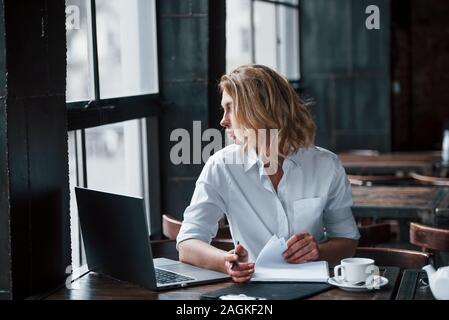 Want to have a walk on the street. Businesswoman with curly blonde hair indoors in cafe at daytime Stock Photo