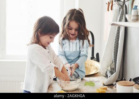 Trying to recreate what they were taught. Preschool friends learning how to cook with flour in the white kitchen Stock Photo
