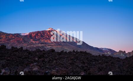 Spain, Tenerife, Volcano mount teide peak in magical red alpenglow sunset light behind endless lava fields Stock Photo