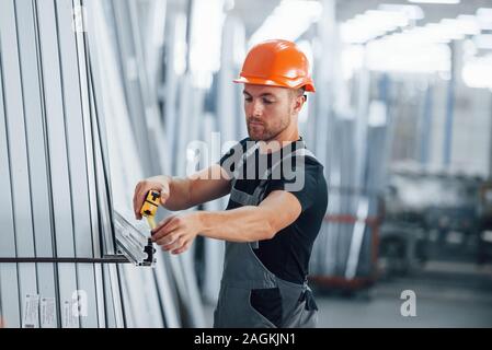 Measuring length of objects. Industrial worker indoors in factory. Young technician with orange hard hat Stock Photo