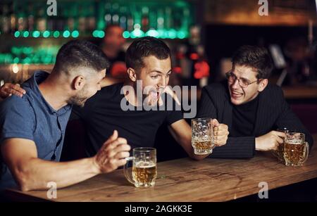 Three friends resting in the pub with beer in hands. Having conversation Stock Photo