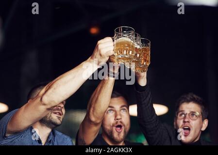 Knocking glasses. Three sports fans in a bar watching soccer. With beer in hands Stock Photo