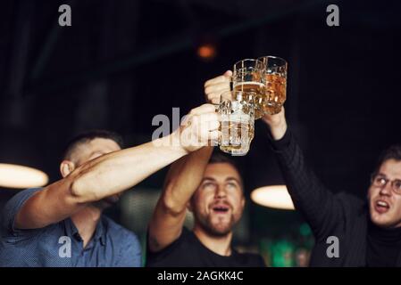 Knocking glasses. Three sports fans in a bar watching soccer. With beer in hands Stock Photo