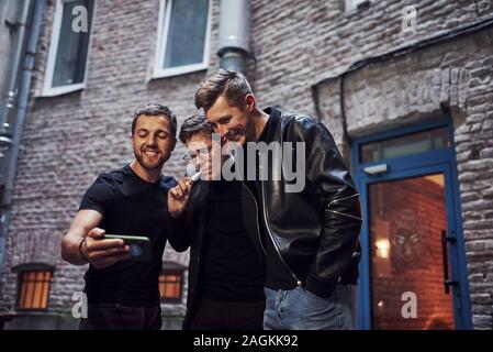 Three male friends stands outside the bar. Having conversation. In nice clothes